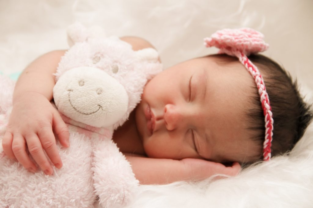 A newborn baby girl sleeping peacefully while holding her teddy bear