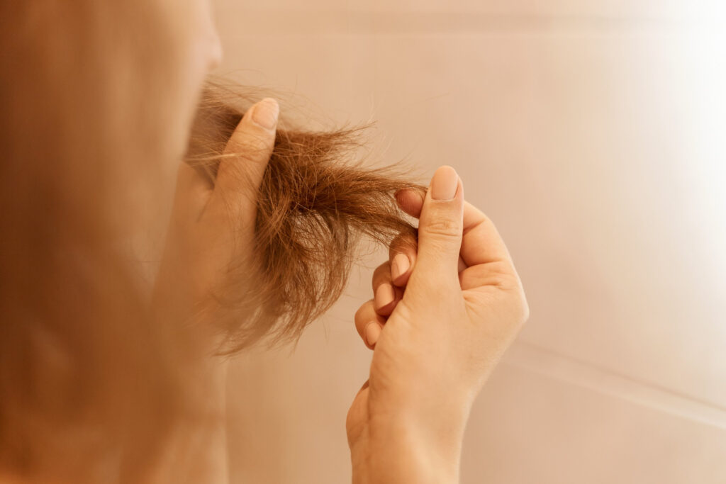 A Young woman holds dry damaged hair ends.
