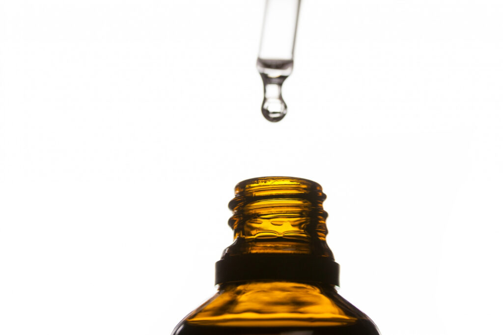A drop of oil dripping from a pipette into a bottle of essential oil
