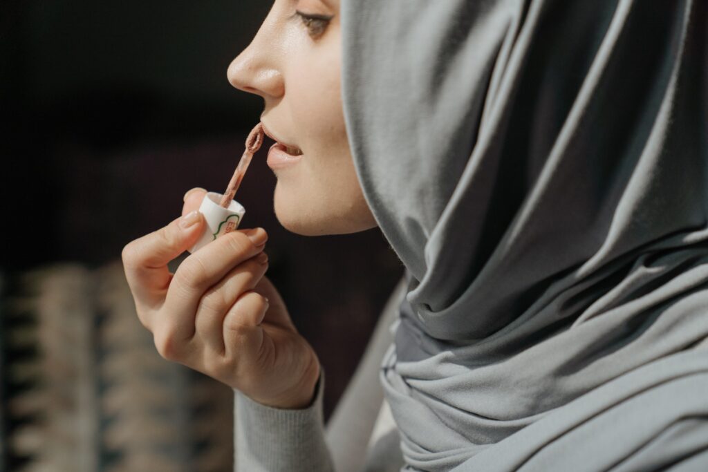 woman in gray hijab applying lip gloss
