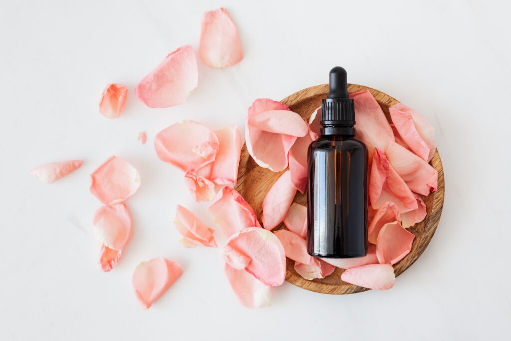 cosmetic bottle with pink rose petals and wooden plate