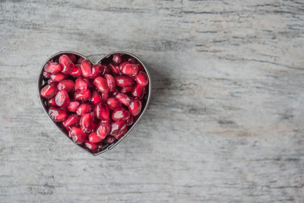 A silver heart bowl full of red pomegranate seeds      
